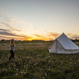 Woman walks toward a glamping tent at sunset on a field at Holmely - Glampingtenten in Central Jutland.