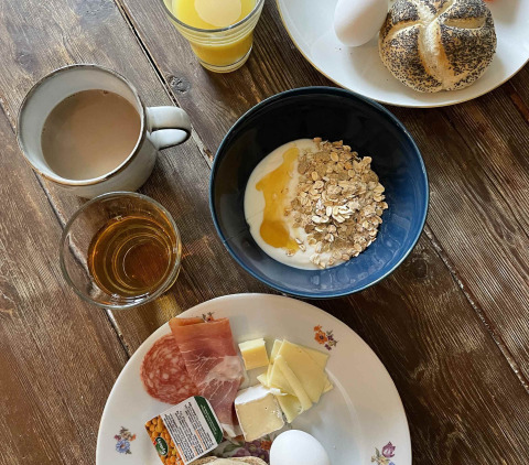 Traditionel morgenmad med yoghurt, ost, pålæg, æg, brød, juice, te og honning på træbord.