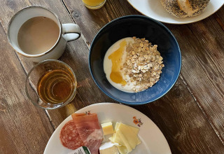 Rustic breakfast with yogurt, muesli, cheese, cold cuts, bread roll, egg, juice, tea and honey.
