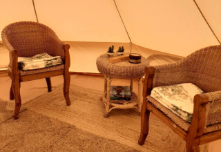 Gemütliche Glamping-Unterkunft mit zwei Korbstühlen, rundem Tisch, Büchern und Decken im Zelt.