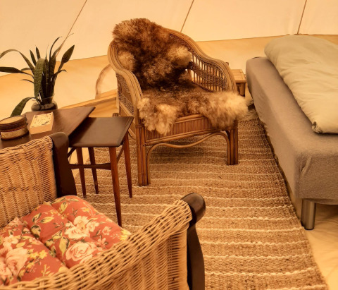 Indretning i glamping telt med kurvemøbler, blød pels, tæppe og planter på Holmely - Glampingtenten Midden-Jutland.