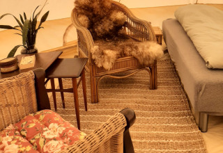 Cozy glamping tent interior with wicker chairs, sheepskin throw, rug, and plant at Holmely - Glampingtenten Midden-Jutland.