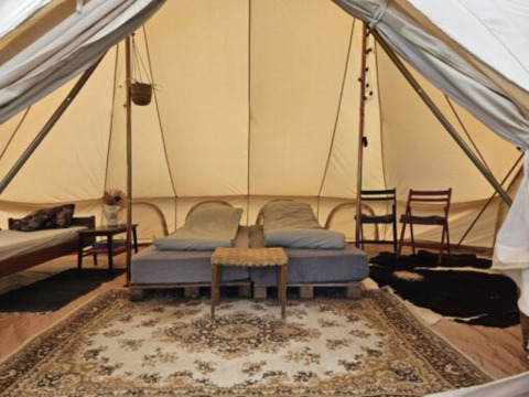 Intérieur d’une spacieuse tente glamping à Holmely, Jutland central, avec lit, tapis et chaises.