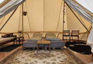 Gezellige inrichting van een glampingtent in Holmely, Midden-Jutland, met bed, vloerkleed en stoelen.