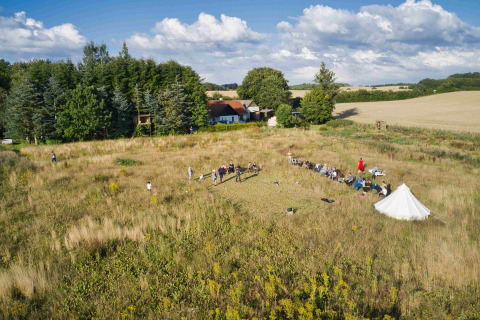 Vista dall’alto di Holmely Glampingtenten in Jutland centrale tra tende e persone in un campo erboso.