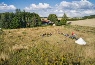 Luchtzicht op Holmely Glampingtenten Midden-Jutland met tenten, veld en aanwezige bezoekers buiten.