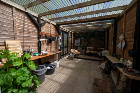 Outdoor kitchen and cozy seating with wood panel walls and clear roof at Holmely glamping tent in Central Jutland.