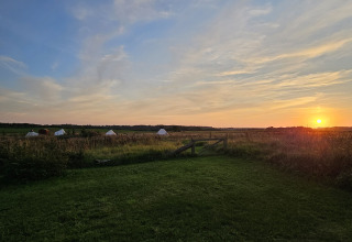 Coucher de soleil sur champ avec tentes glamping Holmely au Jutland central. Portail en bois devant.