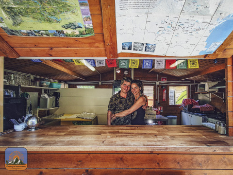 Una pareja sonriente posa en la recepción de Camping des Randonneurs - Yurts Occitanië, rodeados de mapas.