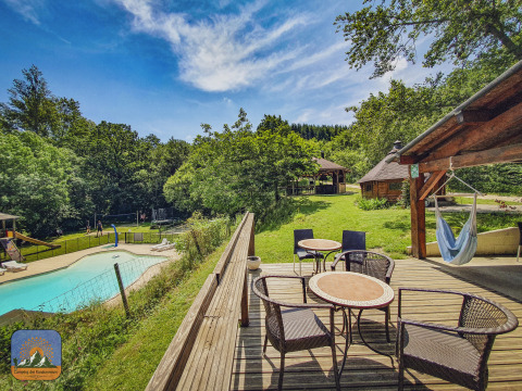 Terrasse mit Sitzmöbeln, Hängematte und Blick auf einen Pool im grünen Camping des Randonneurs.