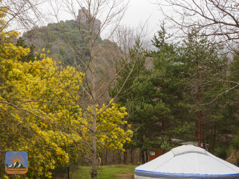 Yurta mongola tradicional en Camping des Randonneurs, rodeada de árboles y una colina con ruinas en Occitania.