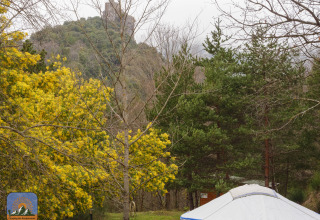 Yurta mongola tradicional en Camping des Randonneurs, rodeada de árboles y una colina con ruinas en Occitania.