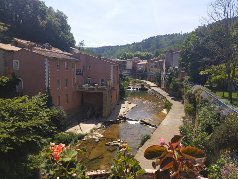 Vue sur la rivière et les maisons près du Camping des Randonneurs - Yurts Occitanië dans une vallée ensoleillée.
