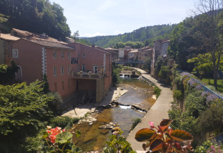 Vista del río y casas cerca de Camping des Randonneurs - Yurts Occitanië en un soleado valle rural.