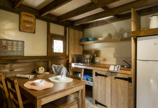 Gemütliche Glampingküche mit Holzmöbeln, Esstisch, offenen Regalen, Kühlschrank und Fenster.