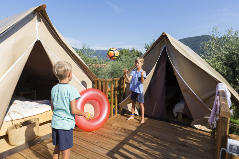 To børn leger med en bold foran glamping telte på træterrasse i Chianti Glamping Resort, Italien.