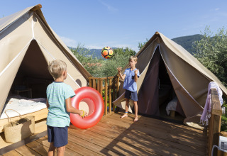To børn leger med en bold foran glamping telte på træterrasse i Chianti Glamping Resort, Italien.