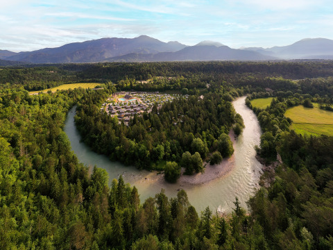 Luftaufnahme von River Camping Bled - Lodges Slovenië mit Fluss, Bäumen und Bergen im Hintergrund.