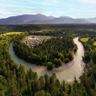 Luchtfoto van River Camping Bled - Lodges Slovenië met rivier tussen bossen en bergen op de achtergrond.