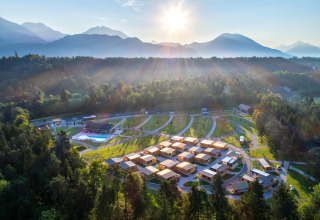 Aerial view of River Camping Bled - Lodges Slovenia glamping site surrounded by forest and mountains.