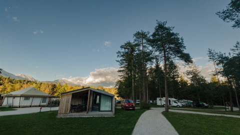 Sfeervolle glampinglodges en campers tussen bomen bij River Camping Bled - Lodges Slovenië, bij zonsondergang.
