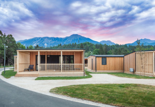 Modern wooden lodges at River Camping Bled - Lodges Slovenië, with mountain views and sunset sky.