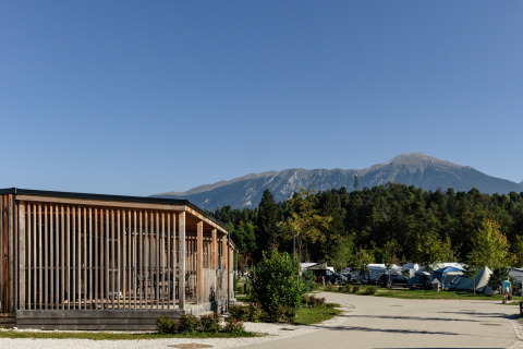 Glamping en River Camping Bled - Lodges Slovenië, cabaña de madera y montañas al fondo, día soleado.