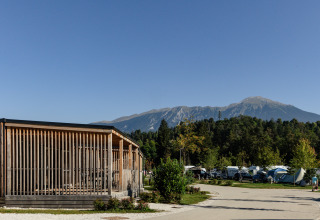 Glamping al River Camping Bled - Lodges Slovenië, lodge in legno e montagna sullo sfondo in giornata soleggiata.