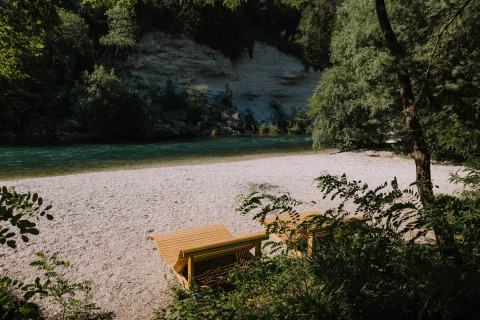 Twee houten ligstoelen aan een rustige rivierstrand bij River Camping Bled - Lodges Slovenië glamping.