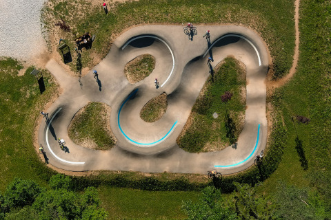 Vue aérienne d'une pumptrack au River Camping Bled - Lodges Slovenië avec des cyclistes et de la verdure autour.