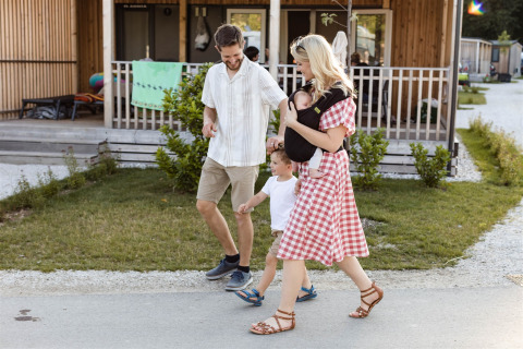 Een gezin wandelt voor hun glamping lodge bij River Camping Bled in Slovenië, baby in draagzak.