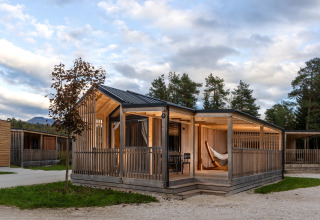 Lodge glamping moderno a River Camping Bled, Slovenia, con veranda in legno e amaca tra gli alberi.