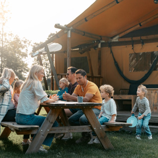 Gezin zit samen aan een picknicktafel bij een luxe glampingtent in Vakantiepark de Italiaanse Meren, Gelderland.