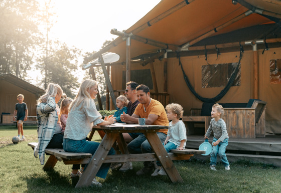 Gezin bij een houten picknicktafel voor een glamping tent op Vakantiepark de Italiaanse Meren in Gelderland.
