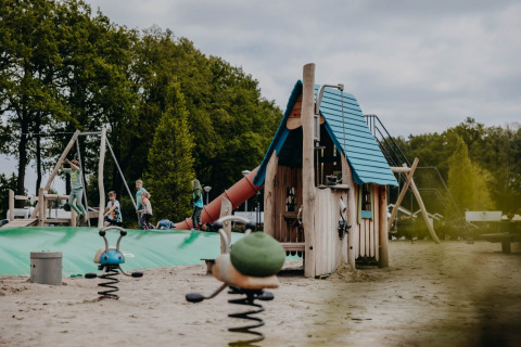 Area giochi per bambini al Vakantiepark de Italiaanse Meren - Glamping Gelderland, circondata da alberi.