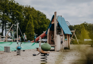 Kinderen spelen op de speelplaats van Vakantiepark de Italiaanse Meren - Glamping Gelderland, omringd door bomen.