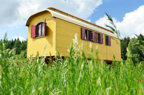 Roulotte jaune pour glamping sur une prairie verte à Hofgut Hopfenburg, Baden-Württemberg, Allemagne.