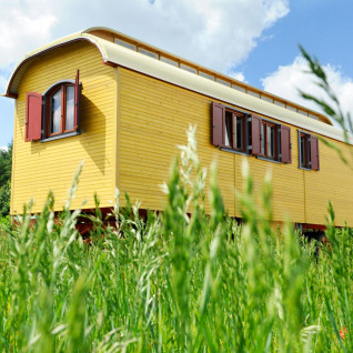 Gele zigeunerwagen voor glamping in het gras bij Hofgut Hopfenburg, Baden-Württemberg, Duitsland.