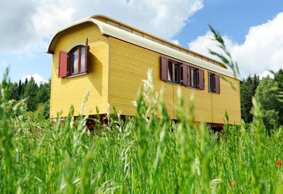 Roulotte jaune pour glamping sur une prairie verte à Hofgut Hopfenburg, Baden-Württemberg, Allemagne.
