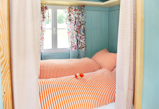 Colorful glamping bedroom with red striped bedding and floral curtains at Hofgut Hopfenburg in Baden-Württemberg.