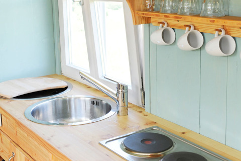 Lyst og hyggeligt køkkenområde i glamping indkvartering på Hofgut Hopfenburg med vask, kogeplade og krus.