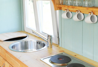 Coin cuisine lumineux dans un hébergement glamping à Hofgut Hopfenburg, avec évier, plaques et tasses suspendues.