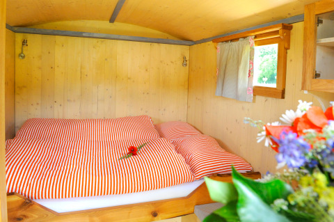 Alojamiento glamping acogedor con paredes de madera, cama de rayas rojas y flores en Baden-Württemberg.