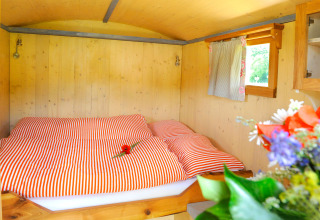 Knusse glampingaccommodatie met houten wanden, rood gestreept beddengoed en bloemen in Baden-Württemberg.