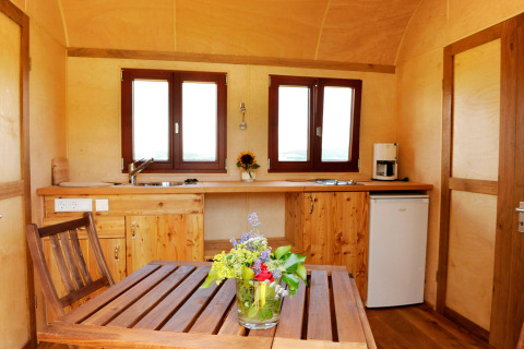 Interieur van glamping accommodatie op Hofgut Hopfenburg met houten keuken, tafel en verse bloemen.