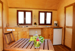 Intérieur d'un hébergement glamping à Hofgut Hopfenburg avec cuisine en bois, table et fleurs fraîches.