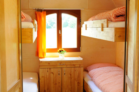 Interior view of cozy glamping accommodation with wooden bunk beds, cabinet, and bright orange curtains.