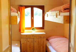 Interior view of cozy glamping accommodation with wooden bunk beds, cabinet, and bright orange curtains.