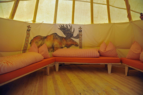 Intérieur d’un tipi avec des coussins orange et lit, fresque d’élan, Hofgut Hopfenburg, Allemagne.
