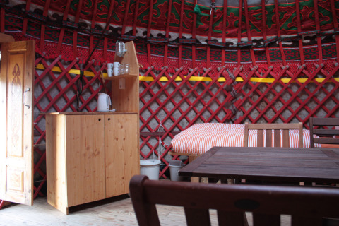 Interior of a cozy yurt with wooden furniture and bed, featured at Hofgut Hopfenburg in Baden-Württemberg.